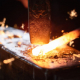 Close-up of hammer and red-hot metal in shape of stick on anvil
